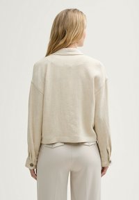 Béžová sako z lněného materiálu s uvolněným střihem, spadlými rameny a knoflíkovými manžetami, s kratší délkou a jemnou texturou.