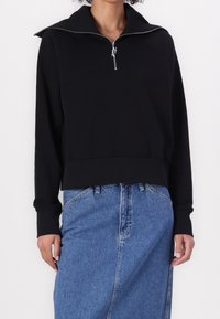 Black zip-up sweatshirt with a high collar, cropped design, and ribbed cuffs, paired with a blue denim skirt. Smooth texture, casual style.
