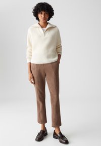 Maglione a maglia crema con collo a zip, abbinato a pantaloni in suede marrone e mocassini neri. Il design presenta una vestibilità comoda e una texture a coste.