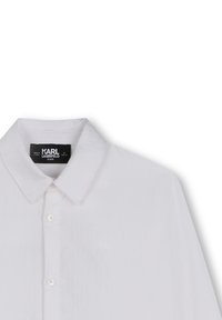Chemise blanche à manches longues avec un col classique, dotée d'un devant boutonné et d'une texture de tissu lisse. L'étiquette indique "KARL LAGERFELD KIDS."