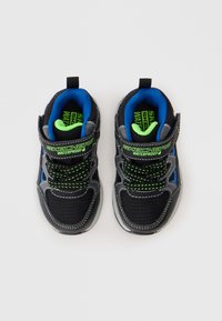 Um par de sapatilhas impermeáveis para crianças, pretas e azuis, da Skechers, com detalhes em verde, atacadores e correias de velcro, vistas de cima.