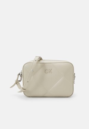 Sac bandoulière rectangulaire beige avec sangle réglable et logo CK embossé à l'avant, texture cuir lisse, design minimaliste.