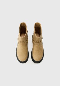 Botas de tobillo de cuero marrón claro con una textura suave, cremalleras laterales, un acento de correa y suelas de goma negras. Vista superior del calzado.