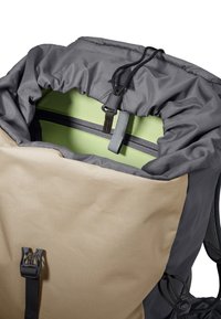 Section supérieure d'un sac à dos beige et gris avec fermeture à cordon coulissant ouverte, montrant une doublure intérieure vert clair et une poche zippée à l'intérieur.