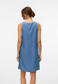 Denim brezrokavnik v svetlo modri barvi, z okroglo izrezom in diskretno odprtino na hrbtu. Ravninska silhueta, dolžina do kolen, minimalno šivanje.