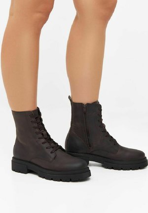 Bottes de cheville en cuir marron à lacets avec une fermeture éclair sur le côté, surface texturée, semelles en caoutchouc épaisses et accents œillets.