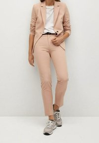 Růžový saka ve světlých odstínech a odpovídající úzké kalhoty v kombinaci s bílým tričkem a šedými teniskami. Hladká tkanina, přizpůsobený design.