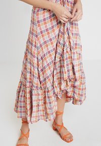 Maxiklänning i lätt, flerfärgad rutigt tyg; har ett lager-på-lager volangkant och frilldetaljer; kompletteras av orangea sandaler med remmar.