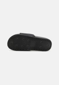 Sandale noire avec une semelle en caoutchouc texturé, dotée d'une large sangle pour le maintien et d'une surface supérieure lisse. Les accents comprennent des clous arrondis.