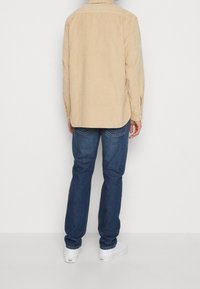 Beige corduroy overhemd met een button-down kraag en lange mouwen, gecombineerd met donkerblauwe jeans en witte sneakers. Eenvoudig ontwerp, zonder patronen.