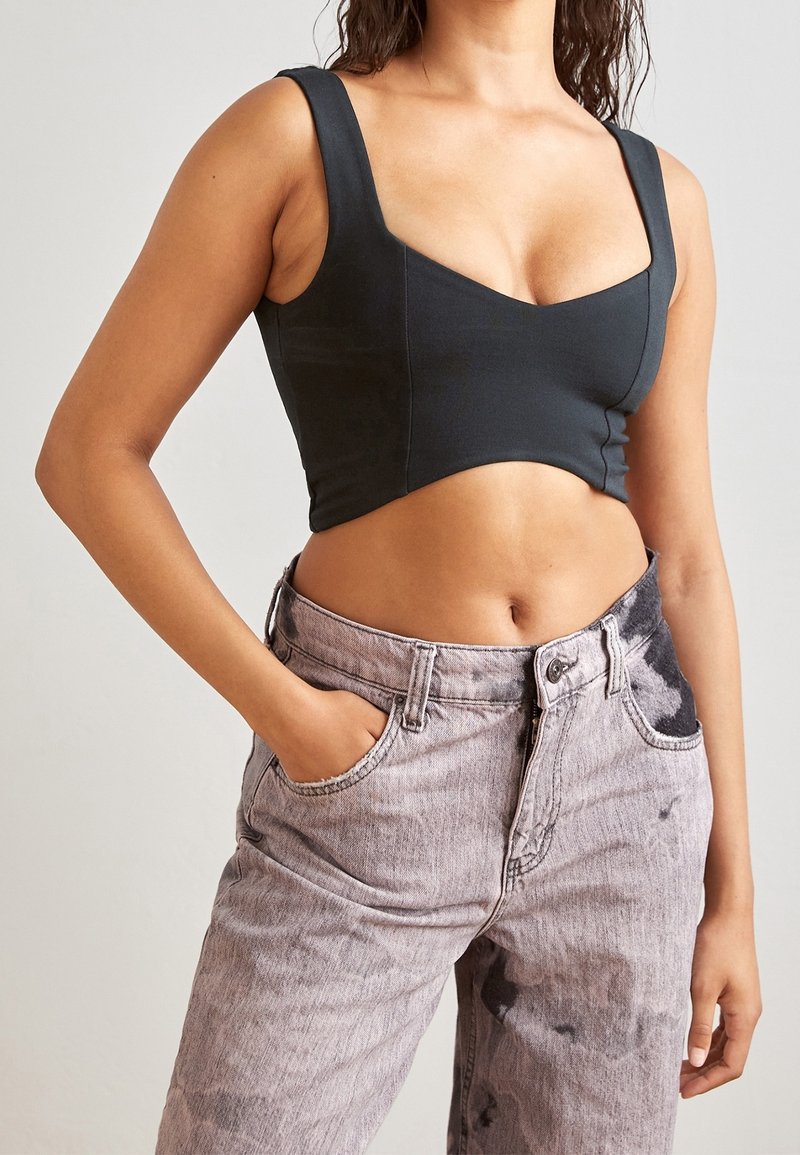 Femme portant un crop top noir et un jean taille haute effet délavé, une main dans la poche, sur fond uni.