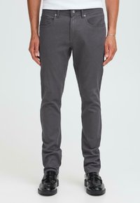 Grijze slim-fit jeans met vijf zakken, gemaakt van een soepele katoenmix, fijne stiksels en metalen knoopaccenten, gecombineerd met zwarte schoenen.