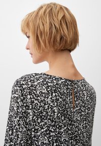 Schwarz-weiße Bluse mit Blumenmuster, runder Ausschnitt und Schlüssellochdetail am Rücken. Weicher Stoff und lockere Passform.