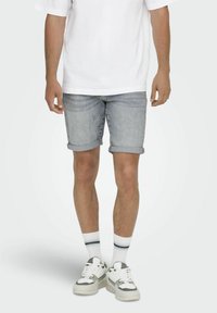 Bermudas de mezclilla azul claro con puños enrollados, combinadas con una camiseta blanca holgada, calcetines deportivos con una línea azul y zapatillas gruesas.