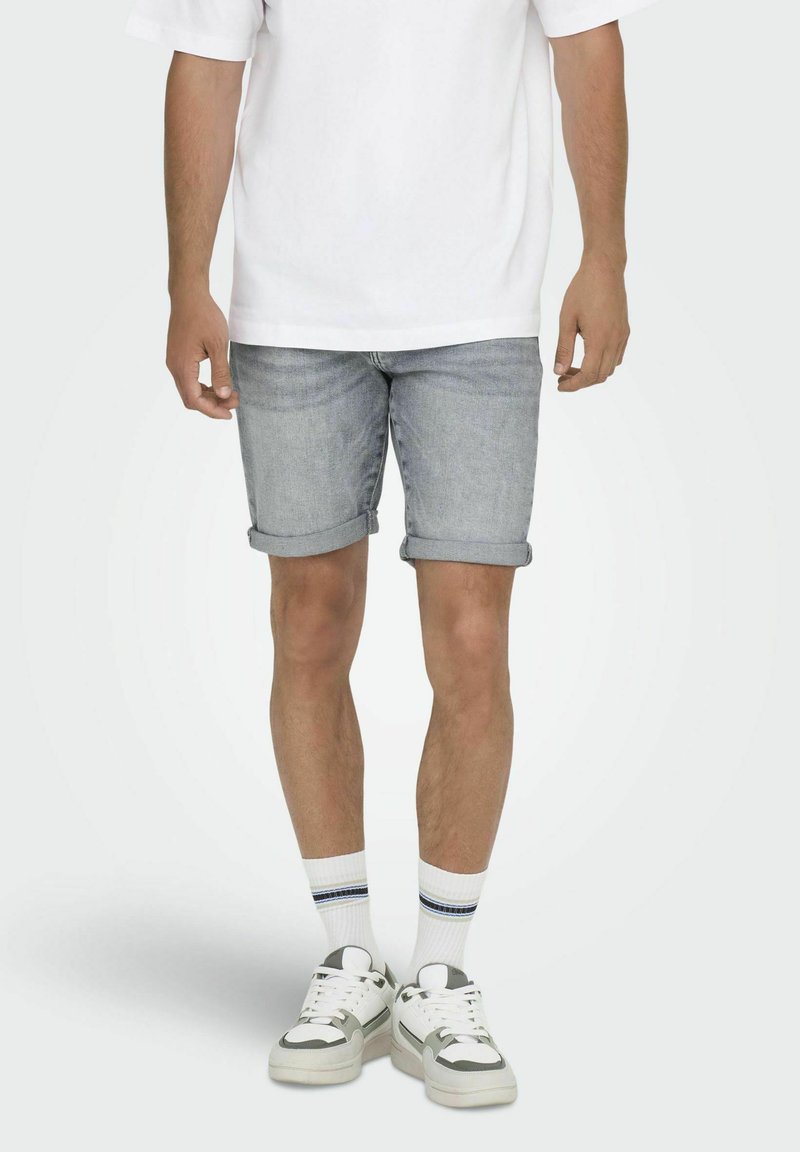 Bermudas de mezclilla azul claro con puños enrollados, combinadas con una camiseta blanca holgada, calcetines deportivos con una línea azul y zapatillas gruesas.
