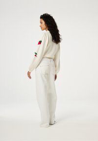 Witte pullovertrui met puffy mouwen, versierd met borduursels van rode aardbeien en groene bladeren, gecombineerd met hooggevoerde, wijde witte jeans.