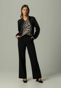 Czarna bomberka z cekinami nałożona na bluzkę w panterkę, w połączeniu z czarnymi spodniami o wysokim stanem i czarnymi szpilkami. Prosty, elegancki design.