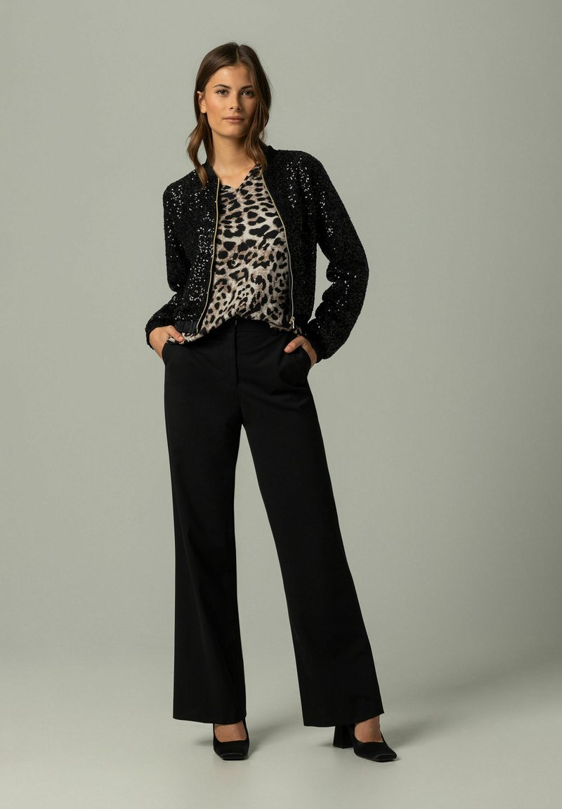 Czarna bomberka z cekinami nałożona na bluzkę w panterkę, w połączeniu z czarnymi spodniami o wysokim stanem i czarnymi szpilkami. Prosty, elegancki design.