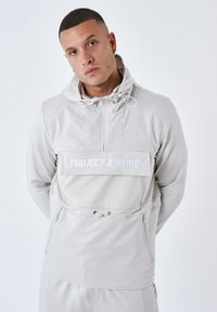 Ljusgrå tröja med huva och dragsko, framficka med dragkedja och "PROJECT X PARIS"-logotyp i vitt. Slät, strukturerad textil.