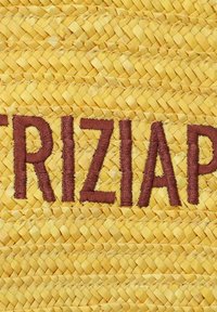 Geel geweven stro met bruine geborduurde letters die "TRIZIA" spellen. De textuur is glad en vlak met een consistent patroon.