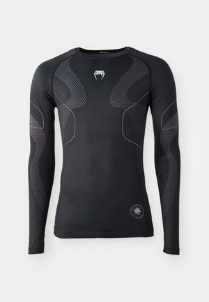 Langærmet sort atletisk skjorte, lavet af strækbart materiale, med kontrasterende grå detaljer og et struktureret mønster på ærmerne og siderne.