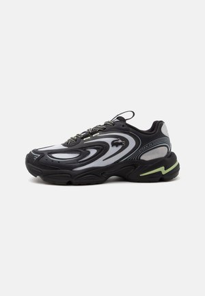 Μαύρο και γκρι sneaker Lacoste Storm 2K με κυματιστά σχέδια, σχεδιασμό με κορδόνια και παχύ πάτο με φωτεινή πράσινη λεπτομέρεια.