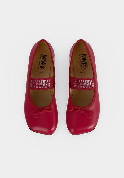 Paire de chaussures rouges en cuir de style Mary Jane avec petits nœuds sur les orteils et bandes élastiques avec des chiffres et un logo entouré d’un six.