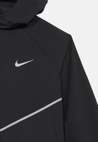 Μαύρο μπουφάν Nike με κουκούλα, με λευκό λογότυπο Nike και διαγώνια αντανακλαστική ταινία στο στήθος και στο μανίκι.