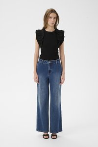 Čierny rebrovaný top s volánovými rukávmi v kombinácii so širokými nohavicami z modrých džínov stredného odtieňa. Modelka má na sebe čierne sandále. Jednoduché pozadie.