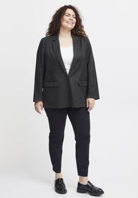 Ciemnoszary blazer z pojedynczym zapięciem na guzik, dwoma przednimi kieszeniami, kołnierzykiem z klapami, zestawiony z czarnymi spodniami i czarnymi butami.