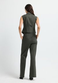 Gilet ajusté vert foncé avec un col haut, associé à un pantalon droit assorti. Le tissu semble structuré avec une texture subtile.