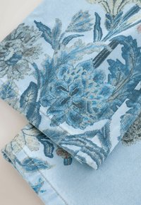 Gros plan d'un tissu bleu clair plié avec un imprimé floral bleu et gris détaillé et des coutures visibles le long des bords.