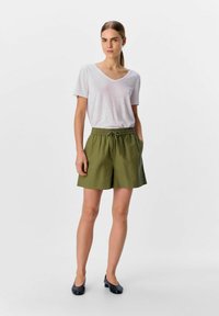 Shorts vert olive avec une taille élastique et deux poches latérales, assortis à un T-shirt à col en V rose clair. Texture du tissu lisse.
