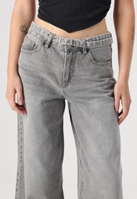 Sive široke jeans hlače iz denima z visokim pasom. Imajo zanke za pas in sprednje žepke. Počasen izgled z sproščenim krojem.