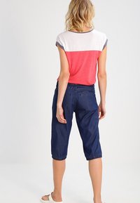Krátké tričko v červenobílé barvě s barevným blokem a krátkými rukávy, ve spojení s tmavě modrými zkrácenými kalhotami se stahovacími manžetami a kapsami.