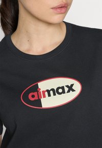 Svart bomull T-skjorte med et fremtredende ovalt logo i rødt og krem, med teksten "airmax" i fete svarte bokstaver.