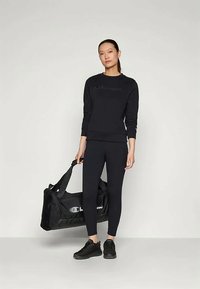 Μαύρη αθλητική μπλούζα με κεντητό λογότυπο, μαύρα κολάν, μαύρα αθλητικά παπούτσια και μια μαύρη αθλητική τσάντα, όλα με κομψή και ομοιόμορφη εμφάνιση.