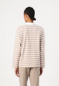 Long-sleeve, beige polo shirt with horizontal stripes in pink and white. The collar is white, and the fabric appears soft and textured.