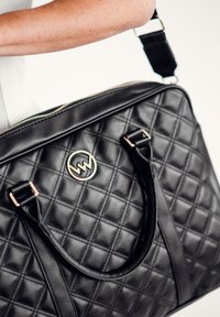 Schwarze gesteppte Lederhandtasche mit einem goldenen runden Emblem, zwei Griffen und einem abnehmbaren Schultergurt. Verfügt über ein diagonales Steppmuster.