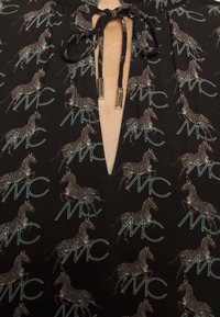 Vêtement noir avec motif répété de zèbres et monogramme "MC", doté d'un décolleté en V fermé par des cordons noirs à embouts dorés.