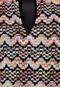 Haut tricoté présentant un motif en zigzag en fils multicolores sur un fond noir, avec un design en V et une texture à mailles ouvertes.