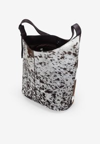 Bolso de hombro de piel de vaca con un patrón manchado en blanco y marrón, textura suave y una correa de hombro de cuero oscuro. Abierto en la parte superior con un bolsillo interior.