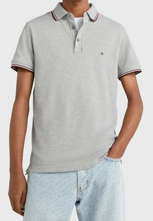 Graues Poloshirt mit Kragen, drei-knopfseitigem Verschluss und kontrastierenden roten und marineblauen Streifen am Kragen und an den Ärmeln.