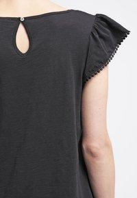 Czarny, krótki top z rękawem z wycięciem w kształcie łezki na plecach, detalami falbanki na rękawach oraz teksturowanym materiałem o subtelnym blasku.