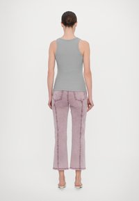 Szary prążkowany top na ramiączkach w połączeniu z jasnoróżowymi, wysokim stanem, dzwonowatymi dżinsami z surowymi wykończeniami i kontrastującymi szwami. Modelka zwrócona tyłem.