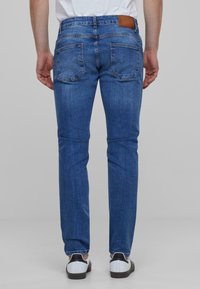 Jeans de mezclilla azul con un corte recto, que presentan un parche de cuero marrón en la cintura y dos bolsillos traseros.