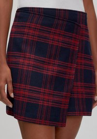 Knie-lange tartan rok in marineblauw en rood, gemaakt van stevige stof. Heeft een wikkelontwerp en een gladde textuur met een afgewerkte rand.