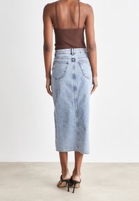 Světlá modrá džínová sukně s vysokým pasem, rovný střih, zadní kapsy a viditelné švy, spárovaná s hnědým tílkem.