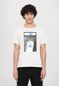 Weißes Baumwoll-T-Shirt mit einem grafischen Druck in Blau, Schwarz und Weiß, der ein Gesicht mit blauen Lippen und Augen darstellt.