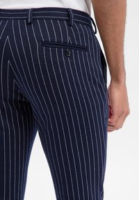 Granatowe spodnie w prążki wykonane z miękkiego materiału, z tylną kieszenią zapinaną na guzik oraz dopasowanym krojem dla eleganckiego wyglądu.